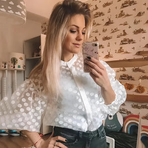White sheer polka dot blouse featuring bishop sleeves, worn by a woman with visible shoulder and neck, styled casually.