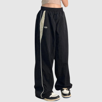 Wide-leg black athletic trousers featuring a contrasting side stripe, designed for sports and casual wear, shown in a unisex fit with an emphasis on comfort and style in size 2XL.