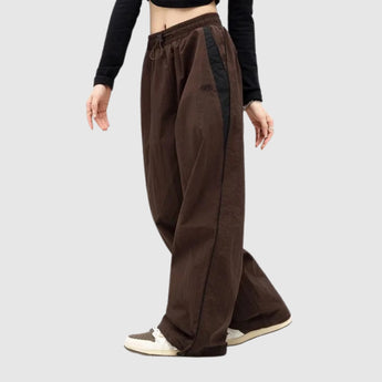 Wide-leg brown athletic trousers with a black side stripe, designed for unisex use, shown in size 2XL. The image highlights the pants' relaxed fit and sporty design, suitable for both athletic and casual settings.