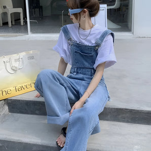 Wide-leg vintage denim overalls with trendy casual chic design, featuring adjustable shoulder straps, front pocket, and relaxed fit, modeled by a person wearing a grey blazer and eyewear.