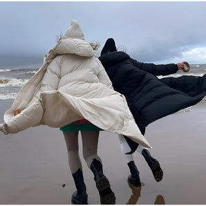 Windproof women's long winter jacket worn by a person outdoors, showcasing the lightweight and waterproof design. The jacket covers the thighs and has long sleeves, suitable for cold and cloudy weather conditions.
