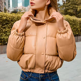 Women's beige cropped puffer jacket, featuring insulated material and a stylish winter design. Displayed is the outerwear garment with emphasis on its fashionable cut, shoulder detailing, and full sleeves, set against a plain backdrop.