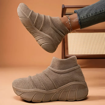 Women's beige high-top sock sneakers placed on a wooden grey flooring, showcasing lightweight and ergonomic design for comfort.