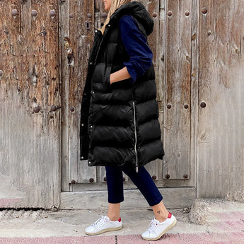 Women's beige hooded puffer vest, sleeveless winter coat, displayed on a person standing, showcasing its fashionable design and waist-length fit.