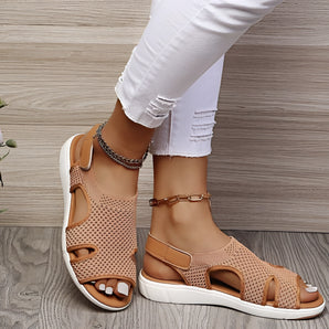 Women's beige mesh sandals with an ankle chain design, styled as comfortable and stylish flats, displayed on a model's foot and leg against a white background.