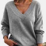 
A woman wearing a gray oversized V-neck sweater, showing the shoulder, neck, and sleeve details, highlighting its cozy and comfortable fit suitable for fall.