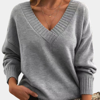 
A woman wearing a gray oversized V-neck sweater, showing the shoulder, neck, and sleeve details, highlighting its cozy and comfortable fit suitable for fall.