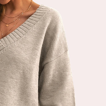 Women's beige oversized V-neck sweater on a mannequin, showcasing the knitwear's wide neckline and loose fit, perfect for a cozy fall look. The sweater covers the shoulders and arms, emphasizing its comfortable and relaxed style.