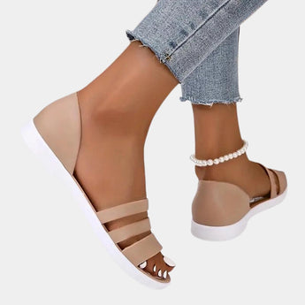 Women's beige strappy flat sandals featuring a pearl ankle bracelet on a person's foot.