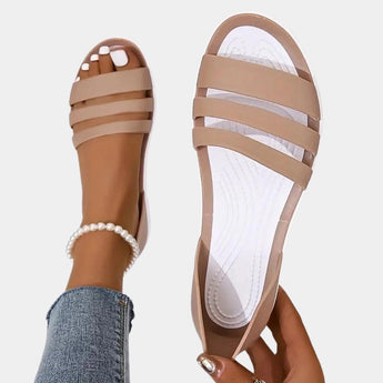 Women's beige strappy flat sandals featuring a pearl ankle bracelet, shown on a person's foot.
