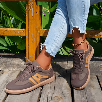 Women's black casual sneakers with a stylish contrast sole, worn by a person standing on grass. The sneakers are paired with brown attire, showcasing a fashionable look suitable for walking.