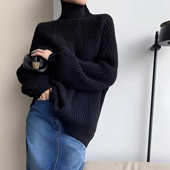 
A woman wearing a black chunky knit oversized turtleneck sweater paired with jeans, standing outdoors with sunglasses on.