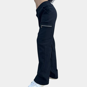 
A woman wearing black high-waist slim fit cargo pants featuring zipper pockets, casually standing with hands on hips.