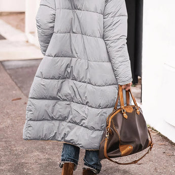 Women's black hooded oversized puffer coat styled for urban street fashion, showcasing its quilted design and relaxed fit with sleeves and waist details visible.