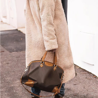 A woman wearing a black hooded oversized puffer coat in an urban street style, showcasing a casual and cozy look. The image focuses on the coat's design and fit, with emphasis on its puffy texture and hooded feature. The coat is styled over casual attire, complementing the urban fashion vibe.