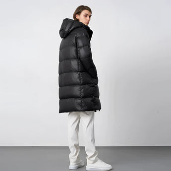 Women's black oversized hooded puffer coat being worn by a model. The coat features long sleeves and a high collar, designed for luxury winter wear.