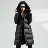 Oversized women's black hooded puffer coat, styled as a luxurious winter jacket, worn by a model who is also wearing sunglasses. The coat features long sleeves and a spacious fit, suitable for cold weather.