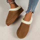 Women's black shearling fuzzy lined platform loafers on a wooden floor with a beige background, showing the shoe's elevated wedge design and comfortable lining.