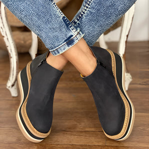 Women's black ankle boots with a stylish zipper design, worn for a casual look. The image focuses on the boots, showing their sleek appearance and comfortable fit.