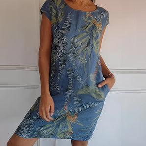 Women's blue floral dress with tropical print, worn by a smiling woman. The dress is a lightweight tunic style, featuring short sleeves and a relaxed fit, in a 5XL size. The garment highlights the shoulders and arms, with a vibrant pattern that stands out against the white background.