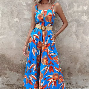 
A woman wearing a blue floral wide-leg jumpsuit with short sleeves and a relaxed fit, perfect for resort fashion. The jumpsuit features a flattering waistline and a stylish neckline, complemented by the wearer's shoulder-length hairstyle.