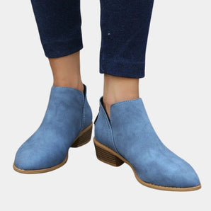 Women's blue suede ankle boots with a pointed toe and mid-heel, styled with denim jeans.