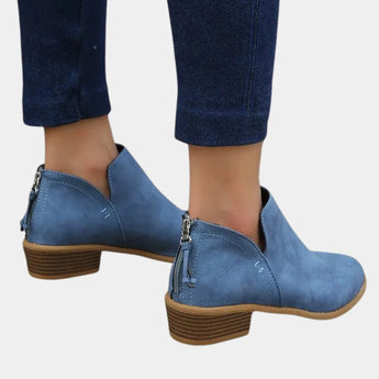 Women's blue suede ankle boots with a pointed toe and mid-heel, worn with dark denim jeans.