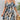 
A woman wearing a blue and white floral cold-shoulder summer dress in size XL, showcasing its elegant design with exposed shoulders and floral patterns.