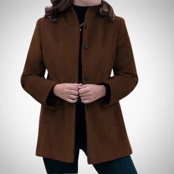Elegant blue wool coat for women, featuring a tailored design and a sophisticated collar. The coat has long sleeves and a classic overcoat style, suitable for winter wear. The color appears to be a mix of blue with hints of grey, adding a unique touch to the garment. The model is showcasing the coat with a confident gesture, highlighting its elegant fit on the shoulders and arms.