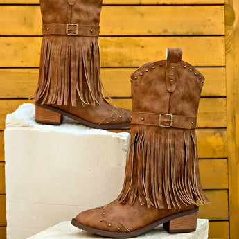 Women's brown suede fringe cowboy booties displayed on a model wearing a dress, highlighting the stylish fringe detail and rich brown color, perfect for fall fashion.