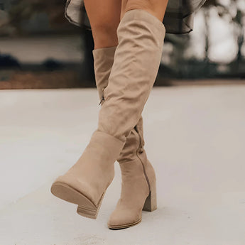 Women's brown suede slouchy knee-high boots in a bohemian fall style, shown on a model standing on a wooden floor, highlighting the knee and calf area.