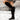 Women's brown suede slouchy knee-high boots in a bohemian fall style, featuring a small hook detail. The boots are showcased on a fashion model, highlighting their knee-high length and stylish design.
