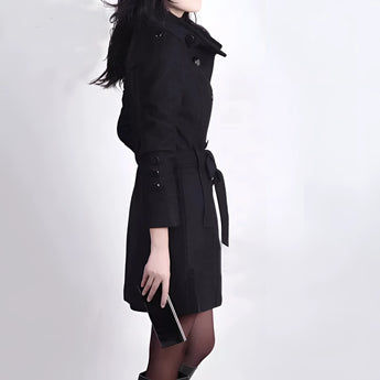 Women's brown wool double-breasted trench coat featuring a stylish design, showcasing elements such as long sleeves, a tailored waist, and a broad collar. The fashion model is displaying the coat's elegant structure with its thigh-length cut and blazer-like details.