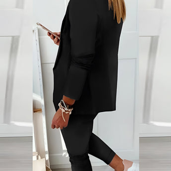 Woman wearing a black blazer, tailored trousers, and white trainers.