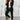 Woman wearing a black blazer, tailored trousers, and white trainers standing with hands on waist.
