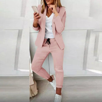 Alt Text: Woman wearing a pink XL business casual blazer and trousers set with a sleek design, featuring a tailored collar, long sleeves, and a dress shirt. She is posing as a fashion model, showcasing the monochrome outfit.