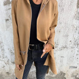 
A woman wearing a lightweight wool camel coat, styled as a casual chic outerwear piece, paired with jeans. The coat features long sleeves and extends to the waist. The model is accessorized with sunglasses and a neutral-toned outfit underneath the coat.