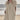 Woman wearing casual linen V-neck beach dress in apricot color, lightweight and short-sleeve, standing on a beach with the sky and water in the background, dress size 5XL.