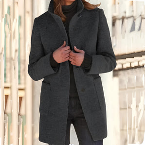 Elegant charcoal gray wool coat for women, featuring a mid-length design with a sophisticated collar and tailored waistline. The coat has long sleeves and is ideal for winter wear, shown in a standing position. Color exhibited is Nero, size 2XL.