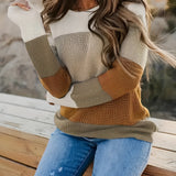A woman wearing a color-blocked cozy knit sweater with trendy tri-color fashion, featuring shades of brown, white, and another color, in size XL. The sweater has long sleeves and a comfortable fit, suitable for outerwear. She is smiling, highlighting the sweater's casual and stylish appearance.