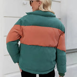 
A woman wearing a color-blocked oversized puffer jacket in green and orange, featuring a high collar and long sleeves for added comfort and warmth.