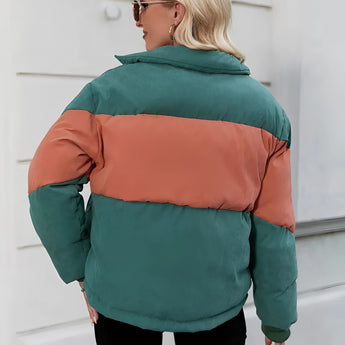 
A woman wearing a color-blocked oversized puffer jacket in green and orange, featuring a high collar and long sleeves for added comfort and warmth.