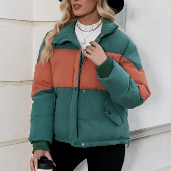 Women's color-blocked oversized puffer jacket in green and orange, featuring a bold design with contrasting sections. The jacket includes long sleeves and an oversized fit, styled with accessories such as sunglasses and a hat.