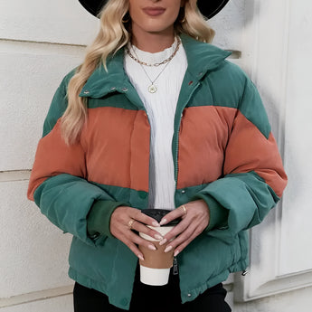 Women's oversized puffer jacket in green and orange color-block, shown in XL size, worn by a model accessorized with a hat and sunglasses.