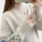 Women's cozy sweater featuring intricate floral embroidery, showcasing a stylish autumn winter fashion design, worn by a model. The sweater has long sleeves and a neckline that adds elegance to the outerwear, in a soft white fabric.