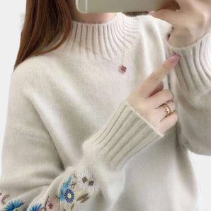 Women's cozy sweater featuring intricate floral embroidery, showcasing a stylish autumn winter fashion design, worn by a model. The sweater has long sleeves and a neckline that adds elegance to the outerwear, in a soft white fabric.