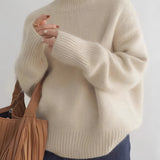 Women's oversized cashmere turtleneck sweater in beige, showcasing long sleeves and a comfortable, cozy fit.