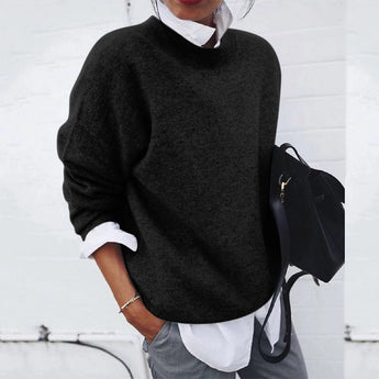 A woman wearing a loose-fitting black knit sweater with long sleeves and a high neck, suitable for fall fashion. She is wearing eyewear and is posed in a way that highlights the sweater's cozy design.