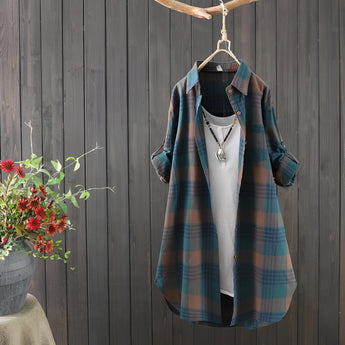 Women's cozy plaid linen dress in grey with tartan pattern, long sleeves, and collar, hanging on a clothes hanger with plants in the background.