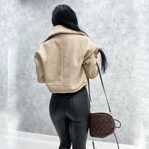 Women's cropped beige leather jacket with fleece collar worn by person, showcasing details like the sleeves, shoulder, waist, and neck area. The jacket's beige leather material and soft fleece collar are highlighted, with a glimpse of grey bag complementing the overall style.